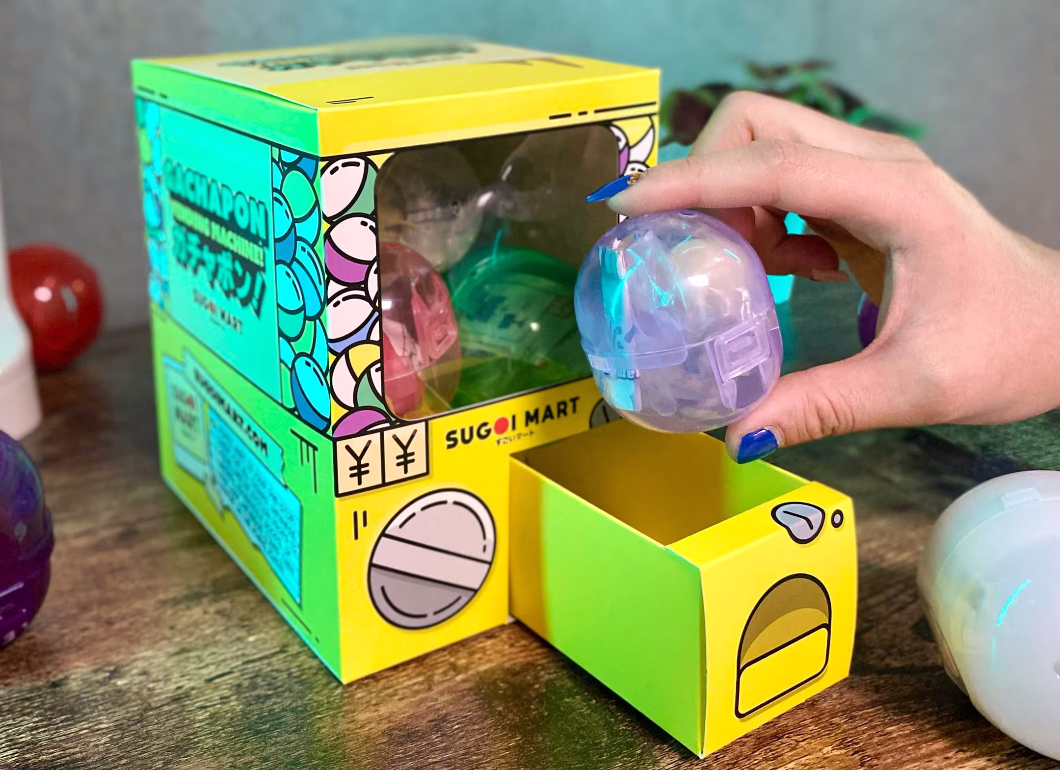 A packaged designed to look and operate like a Japanese gachapon machine, covered in vibrant illustrations and is filled with mini gachapon toys.