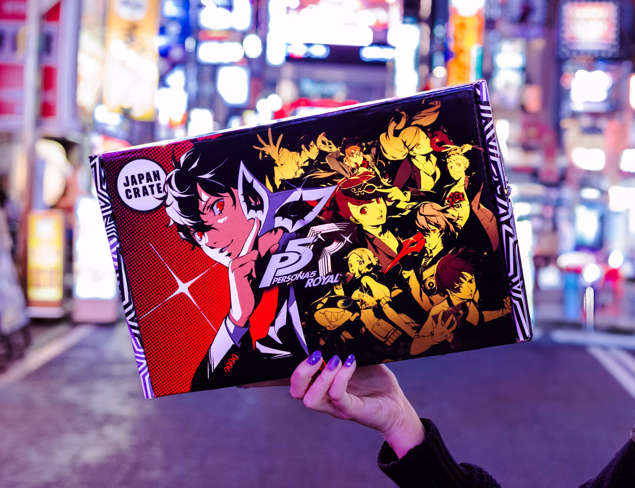 A package featuring art and branding from Persona 5, the video game published by Atlus and Sega. The package is photographed on a Tokyo street which is showcased in the vibrant background.