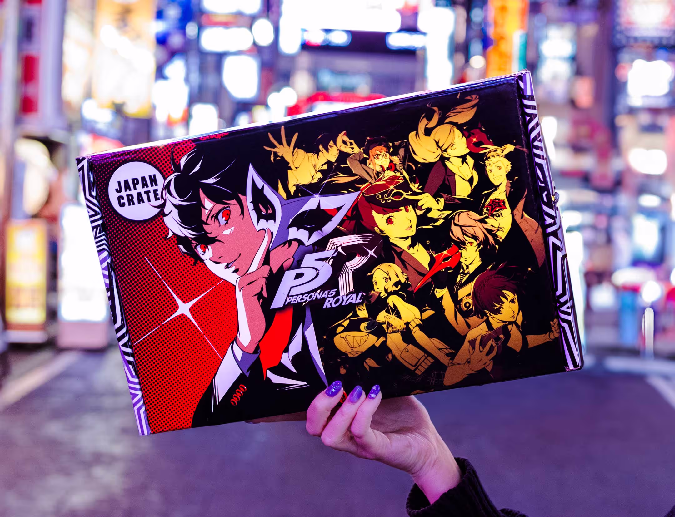 A package featuring art and branding from Persona 5, the video game published by Atlus and Sega. The package is photographed on a Tokyo street which is showcased in the vibrant background.